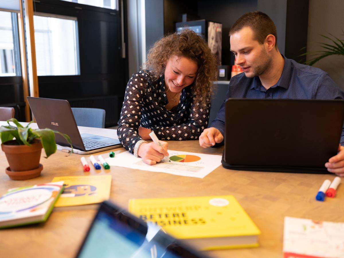 Twee studenten overleggen samen en schrijven op papier