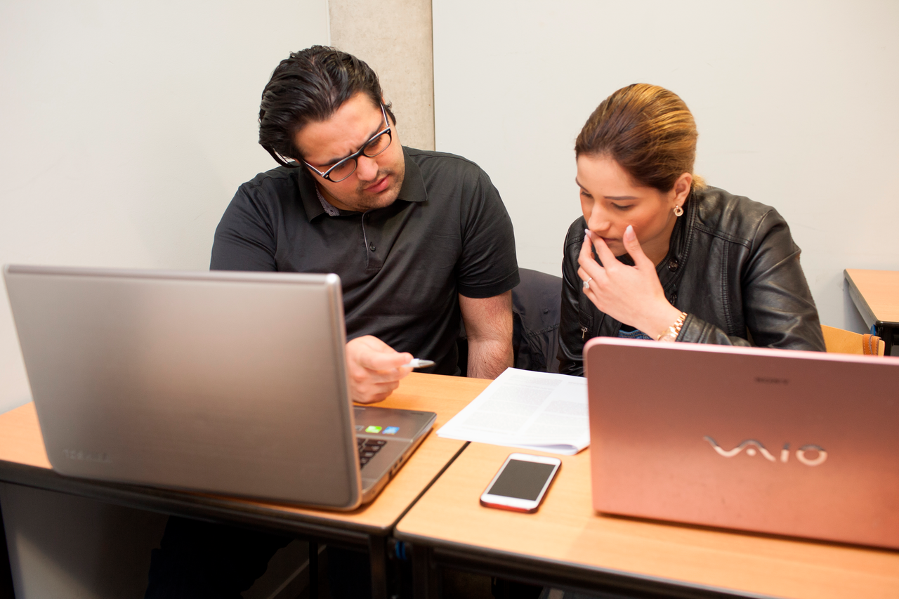 Twee studenten overleggen in les achter laptops