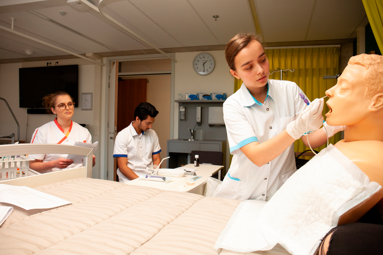 Drie studenten werkend in zorgjassen aan pop in ziekenhuisbed