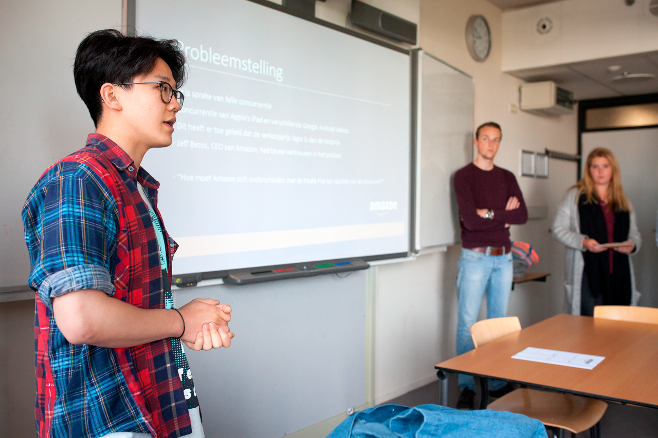 Drie studenten presenteren voor de klas op een scherm