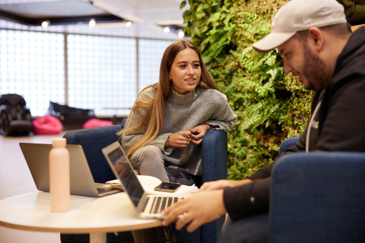 Twee studenten overleggen achter laptops