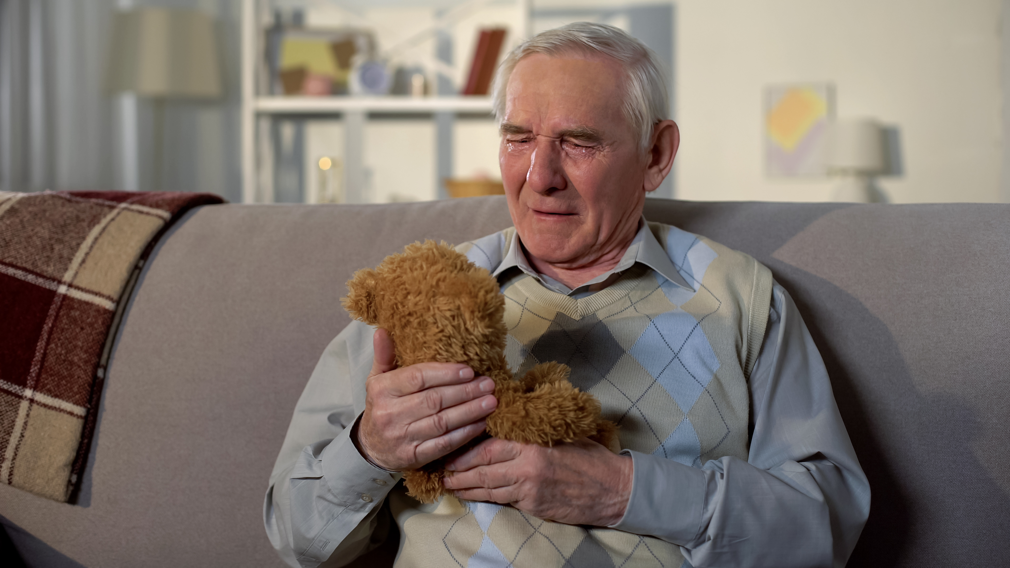 An elderly man crying with a teddybear in his hand