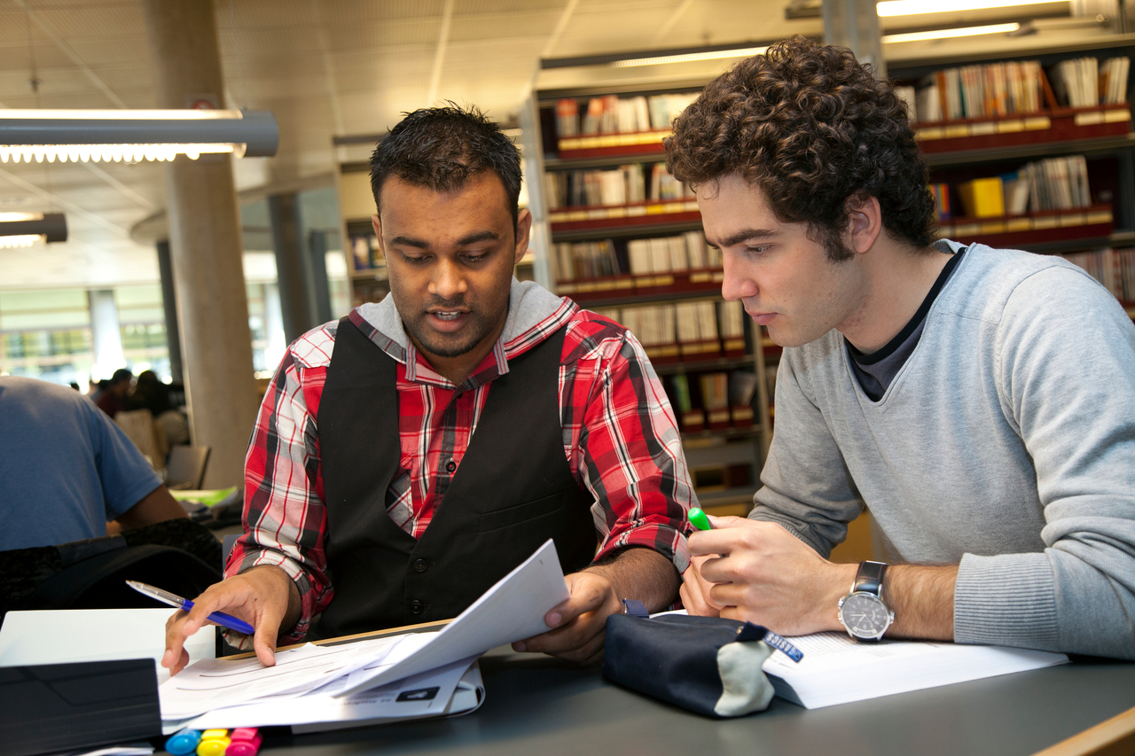 Twee studenten overleggen aan tafel in de bibliotheek