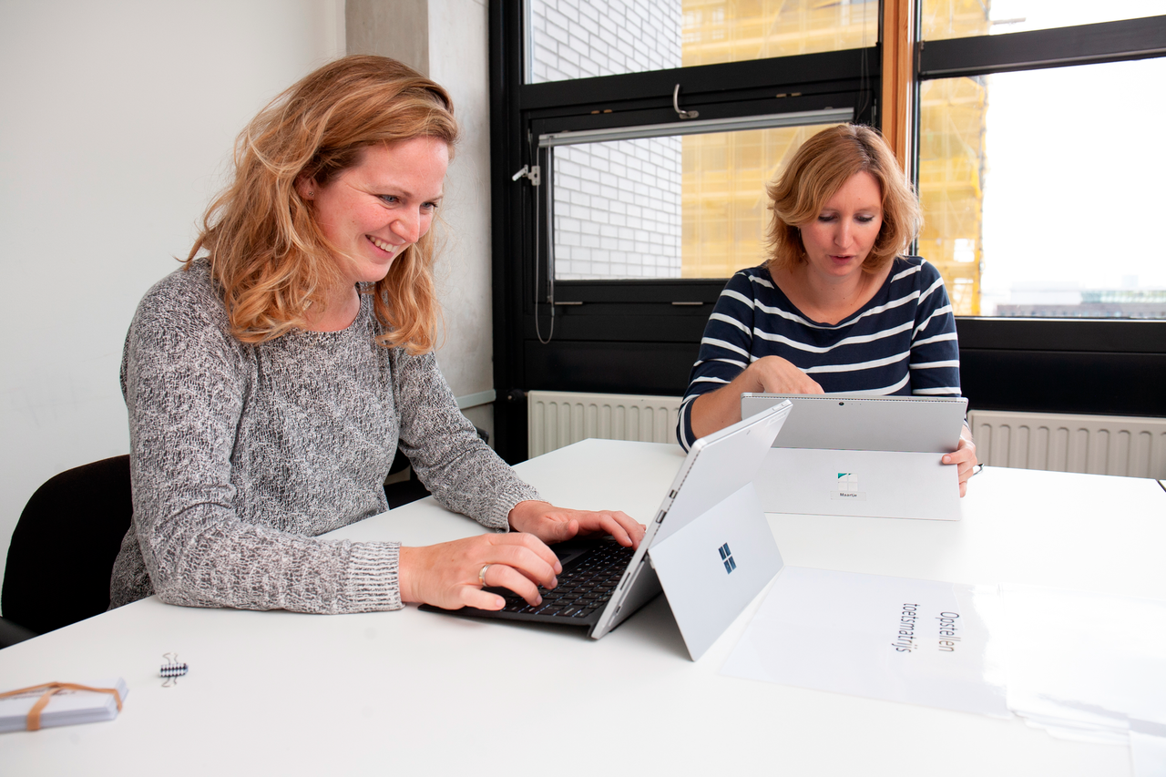 Twee vrouwen zitten om tafel achter tablet