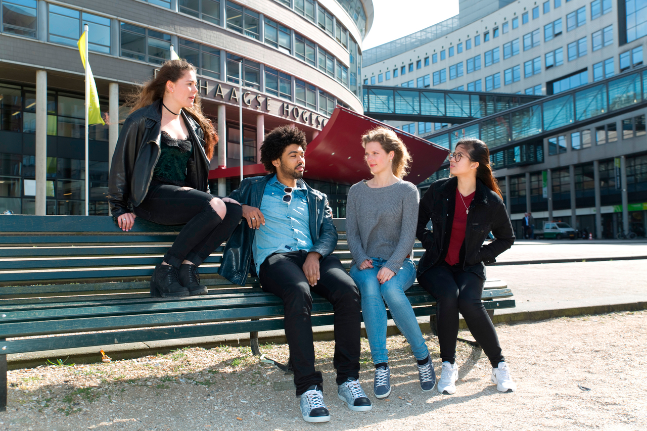 Een groepje studenten zit op een bankje voor de ingang van de hoofdvestiging