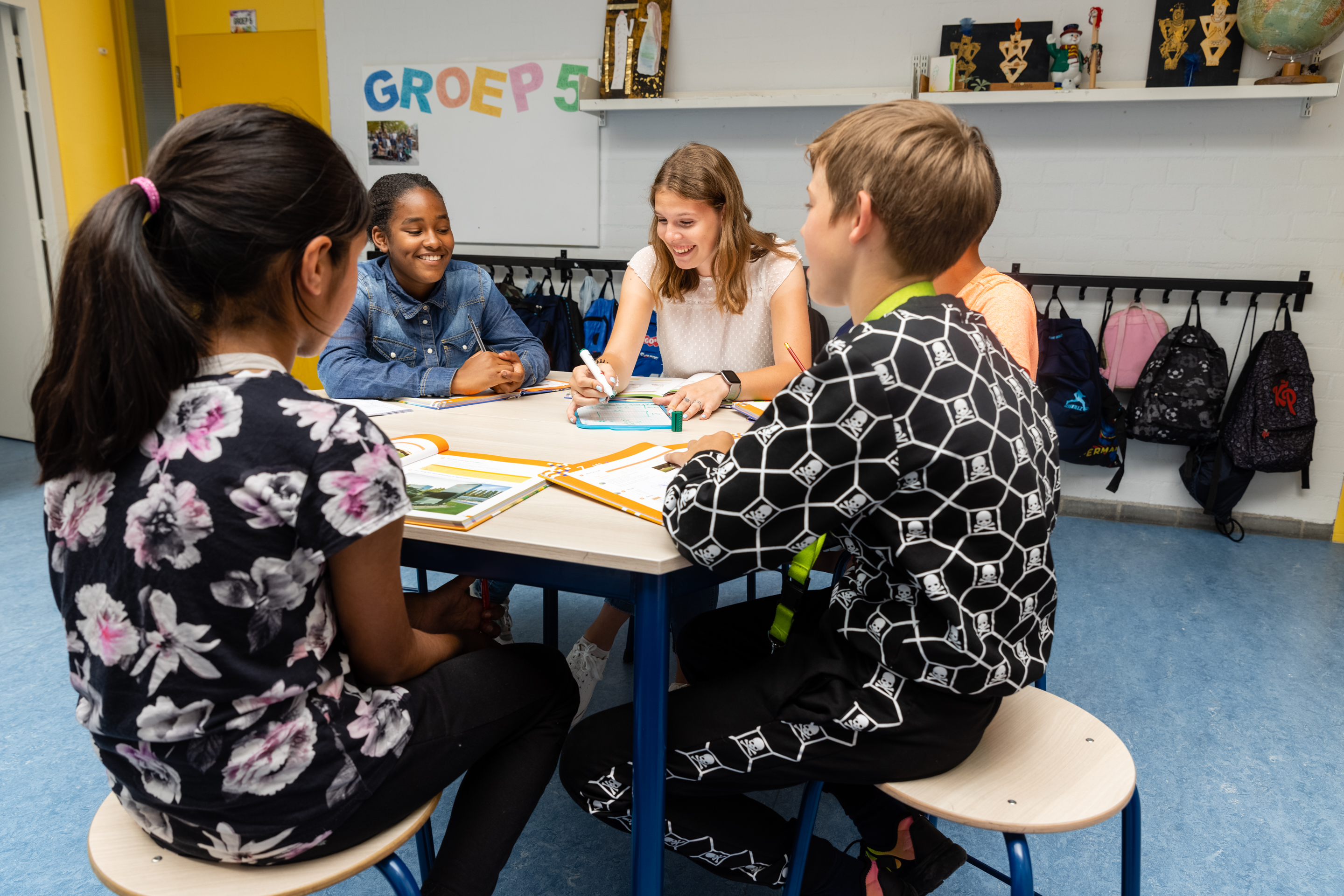 Pabo student zit met kinderen rond tafel in de klas