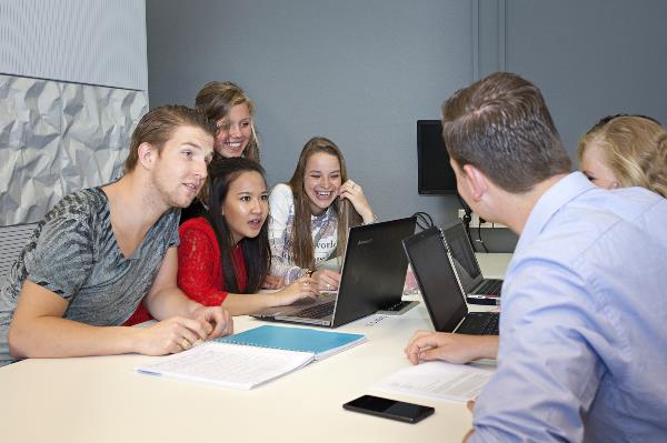 Zes studenten kletsen achter bureaus met laptops