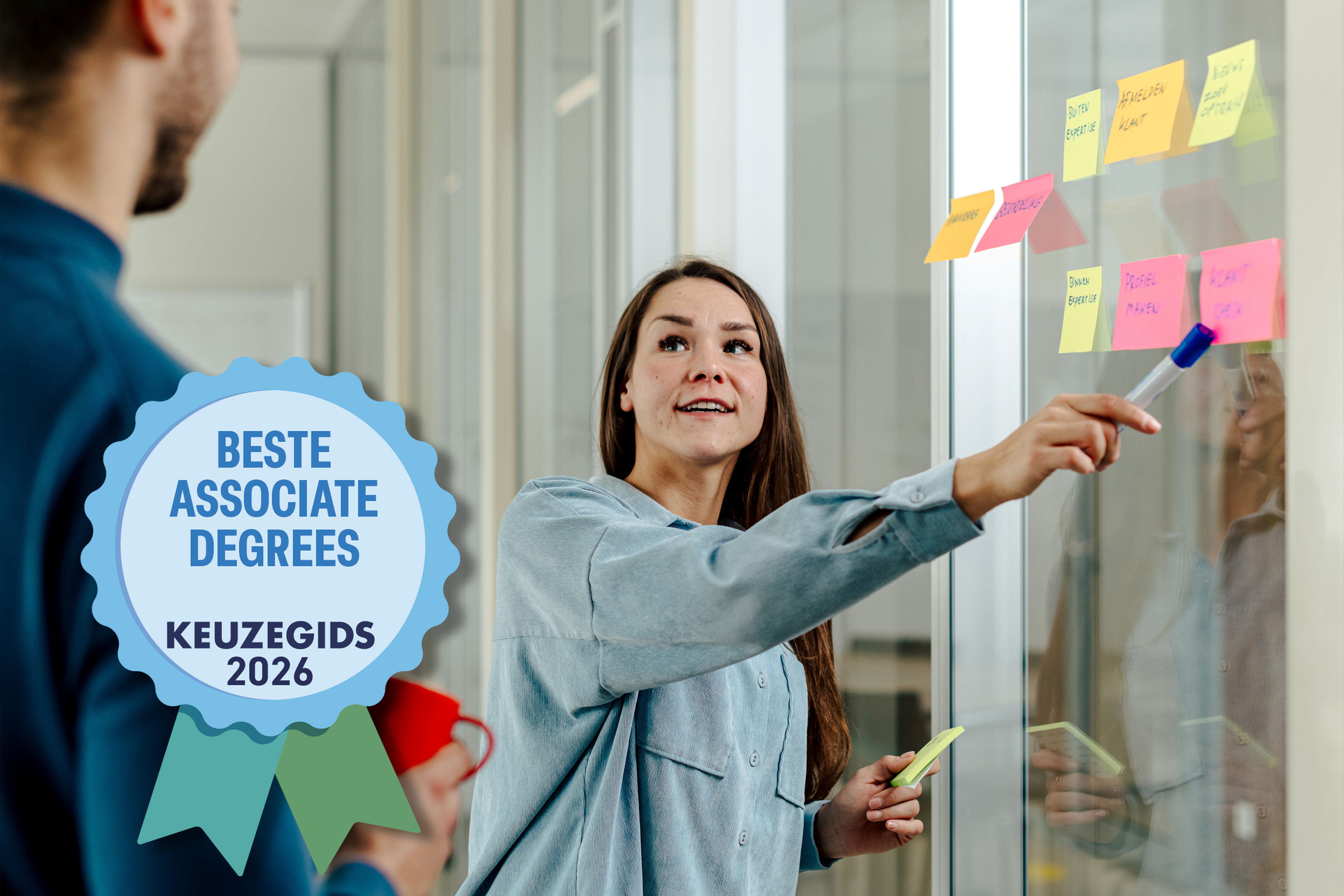 Vrouw wijst naar post-its op glazen muur tijdens overleg; logo "Beste Associate Degrees Keuzegids 2026" staat op de voorgrond.