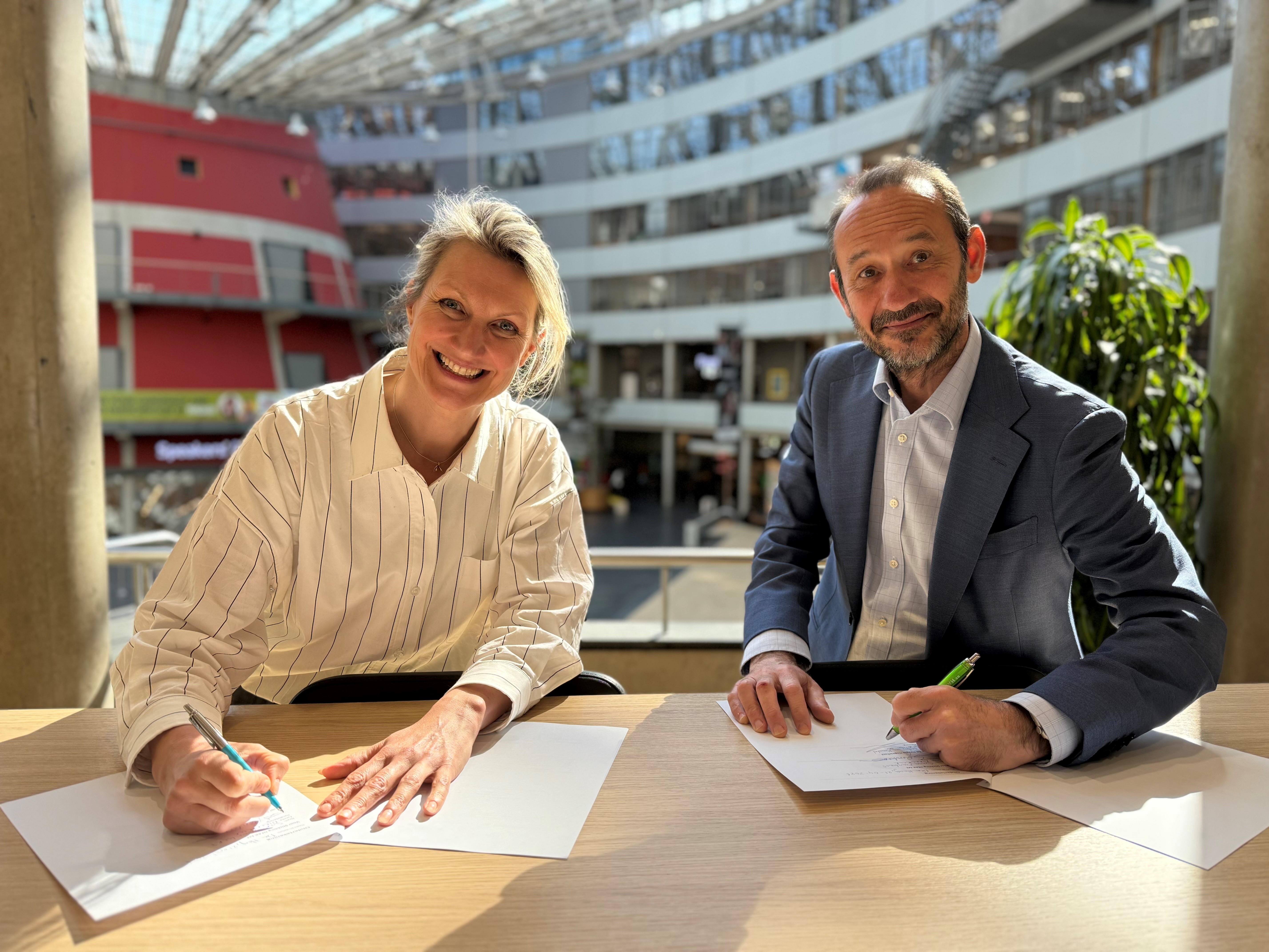 Twee personen zitten aan tafelen om een document te ondertekenen.