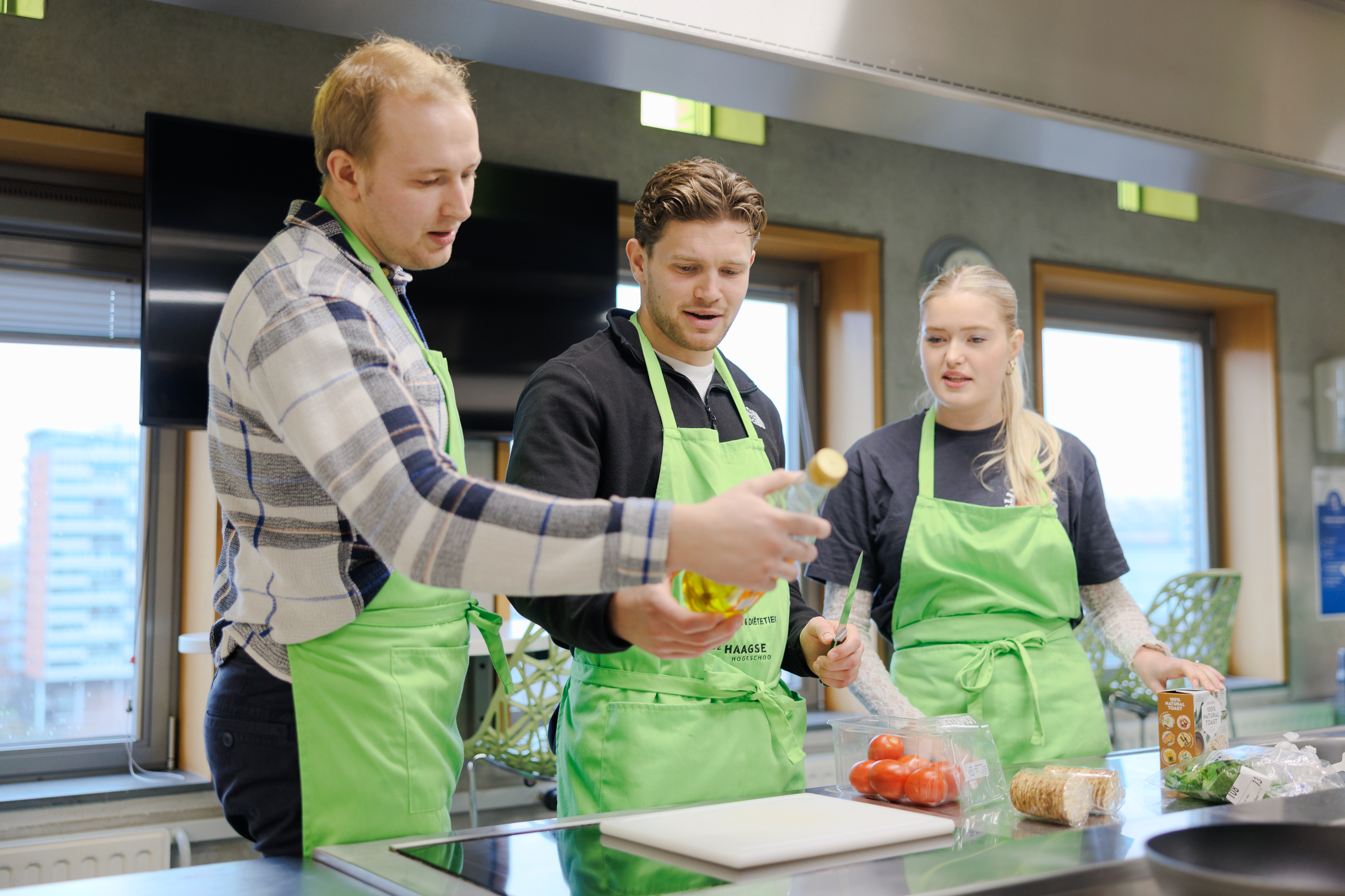 Drie mensen dragen groene schorten en staan samen in een moderne keuken. 